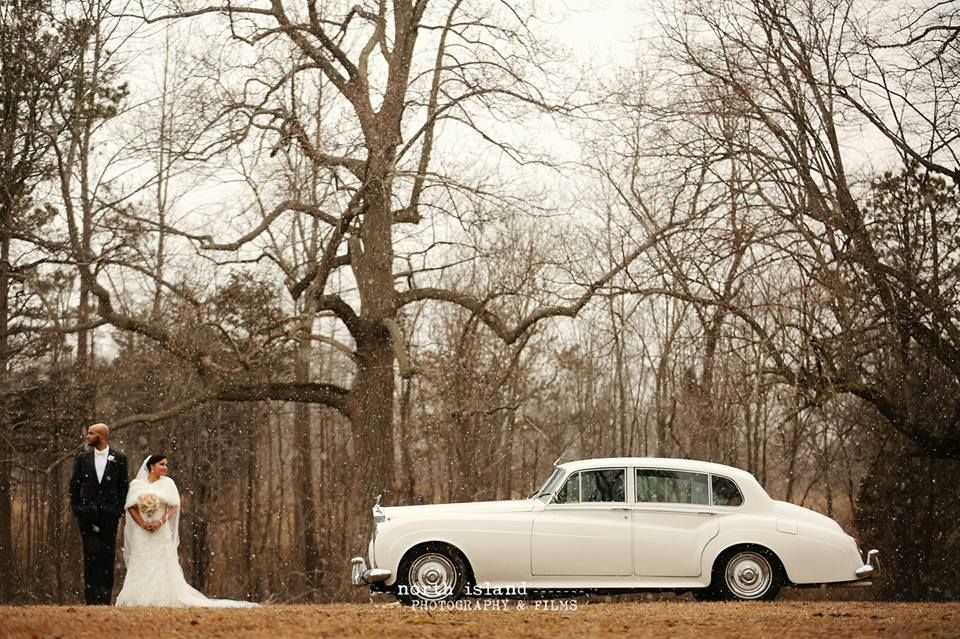 A bride and groom are sitting in the back seat of a car holding champagne glasses.