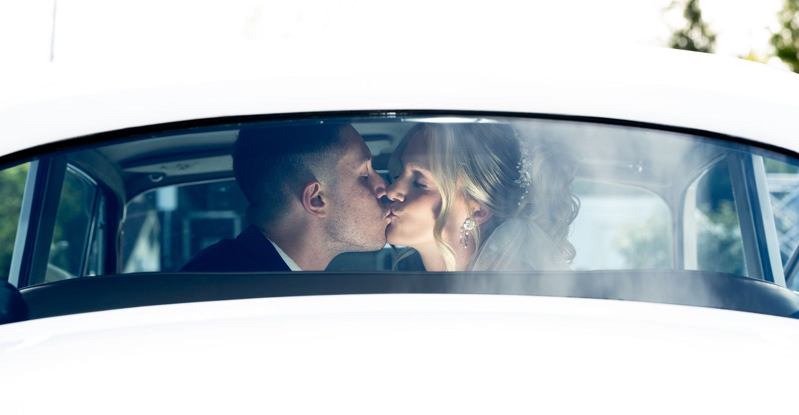 A bride and groom are sitting in a white car.