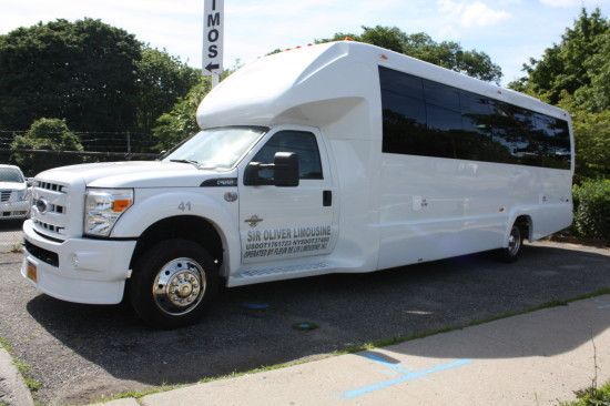 A white limo bus is parked on the side of the road