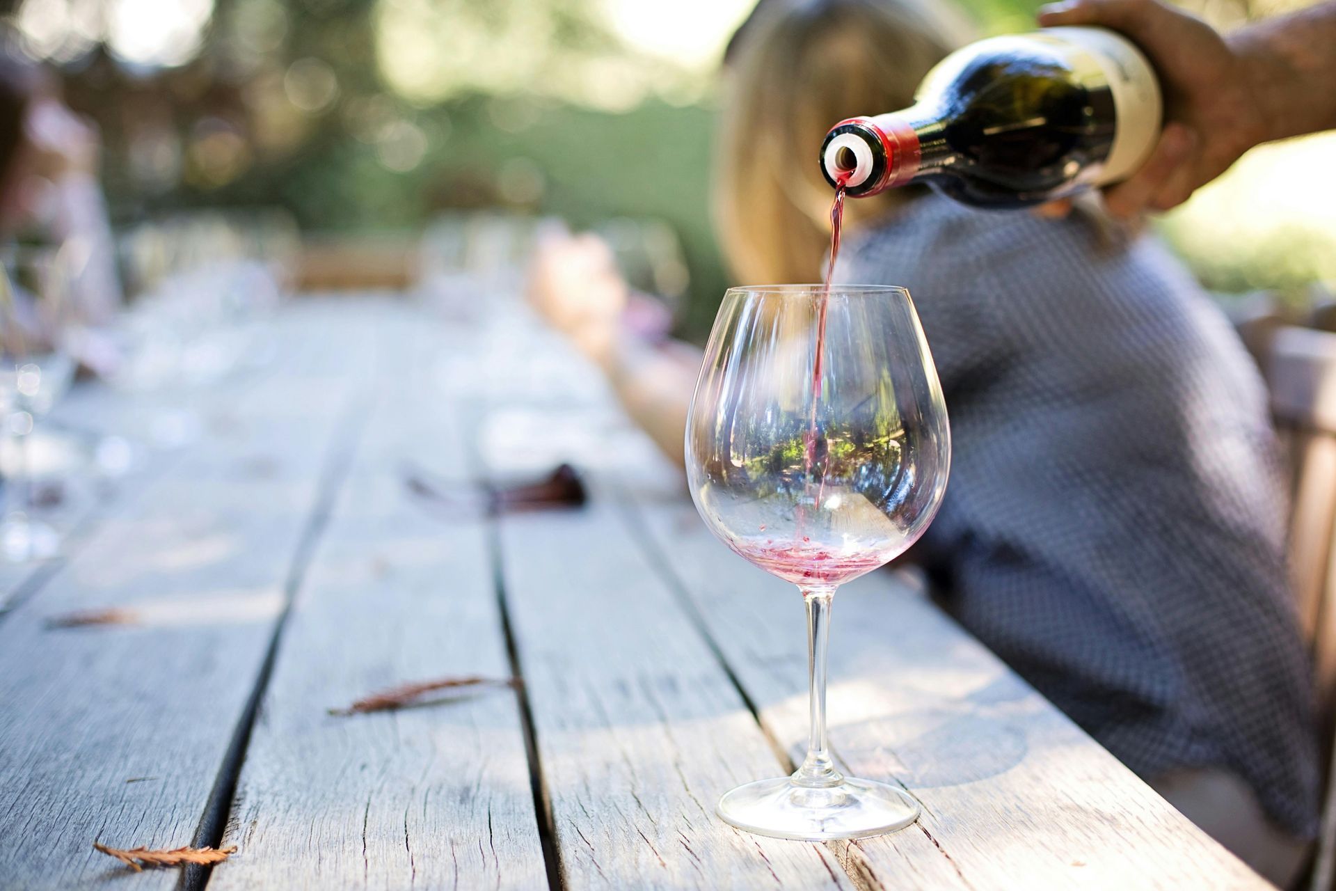 A person is pouring wine into a glass on a wooden table.