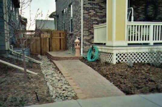 Brick walkway leading to a porch, with a wooden fence and landscaping.