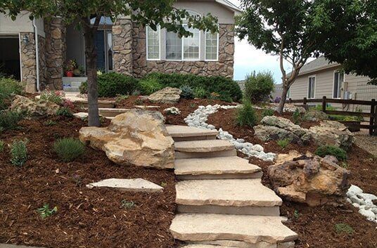 Stone steps leading up to a house with a rock and mulch landscaped yard.