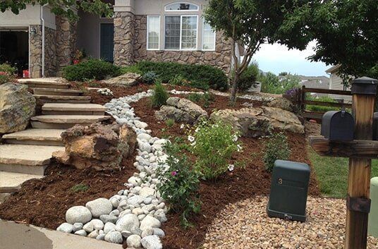 Front yard landscaping with stone steps, river rock bed, and plants.
