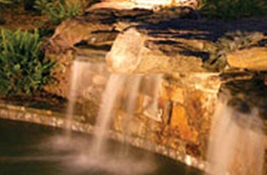 Waterfall cascading over layered rocks, illuminated with warm lighting at night.