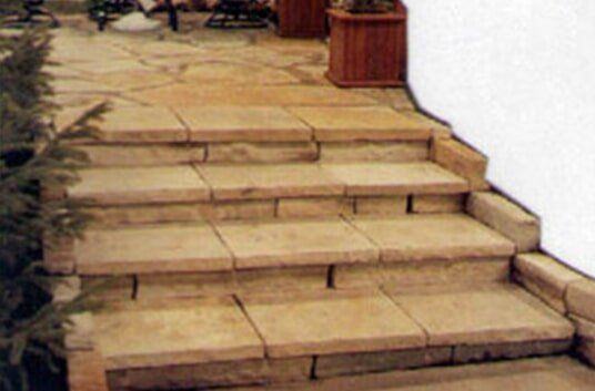 Stone steps leading up, with a low wall on the right and greenery on the left.