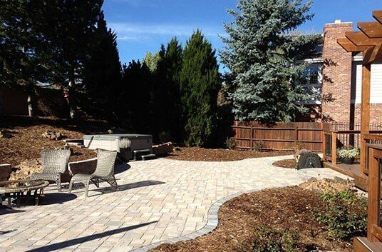 Patio with chairs, hot tub, and landscaping, against a house with a wooden pergola.