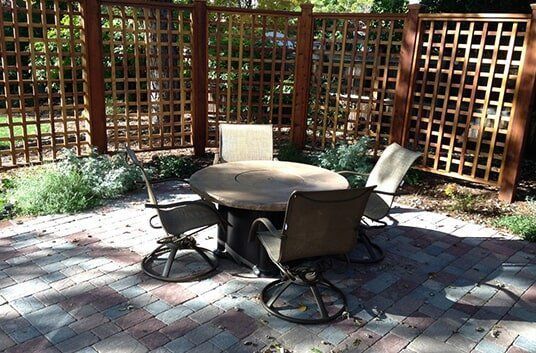 Outdoor dining set with chairs and table on a brick patio surrounded by a wooden trellis fence.