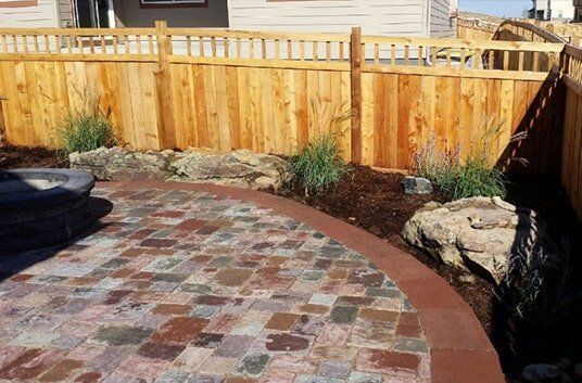 Brick patio with a curved border, surrounded by a wooden fence and landscaping.