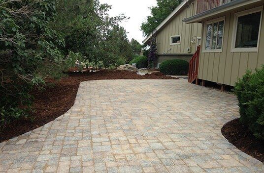 Paver patio next to a tan house with landscaping and mulch border.