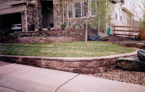 Stone-faced house with lawn and retaining walls. A driveway curves in front of the house.