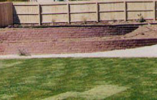 Green lawn leads to a terraced brown retaining wall under a wooden fence.