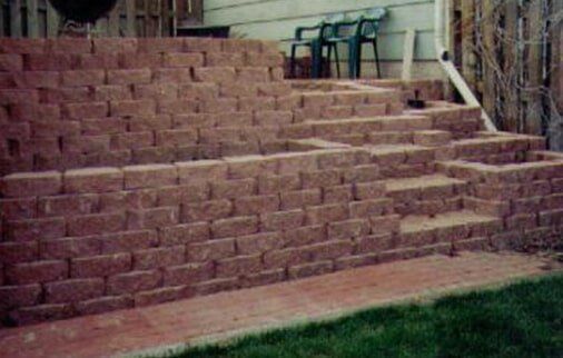 Brick retaining wall with steps leading up to a yard. Brown bricks, green grass.