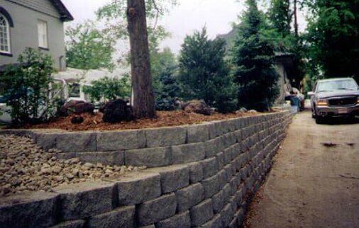 Stone retaining wall bordering driveway with landscaping and a parked vehicle.