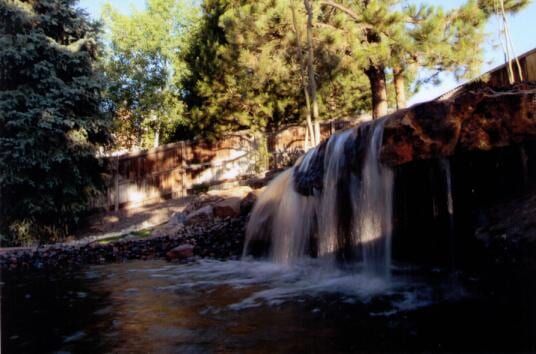 Waterfall cascading into a pool, framed by trees and rocks. Sunlit.