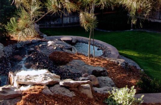 Waterfall feature with a pond surrounded by rocks and greenery.
