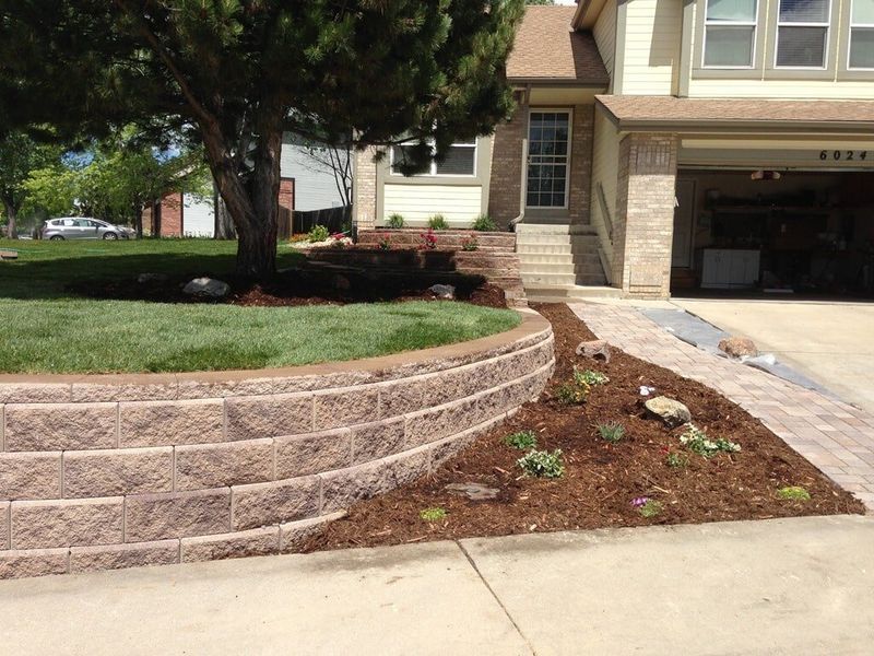 Stone retaining wall and landscaped front yard of a house with a driveway.