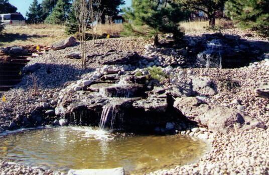 Waterfall cascading into a pond, surrounded by rocks and gravel. Brown and tan color palette.
