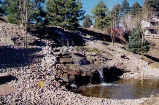 Waterfall cascading into a pond, surrounded by rocks and trees.