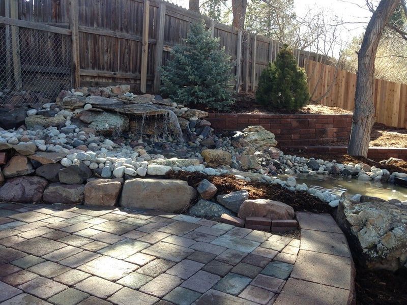 Green lawn in front of a house with a stone exterior and a flower bed with various colorful flowers.