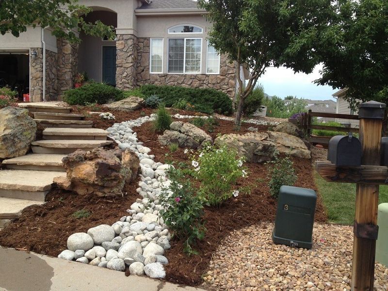 Stone steps lead to a house with a rock and mulch landscaped front yard, featuring a dry creek bed.