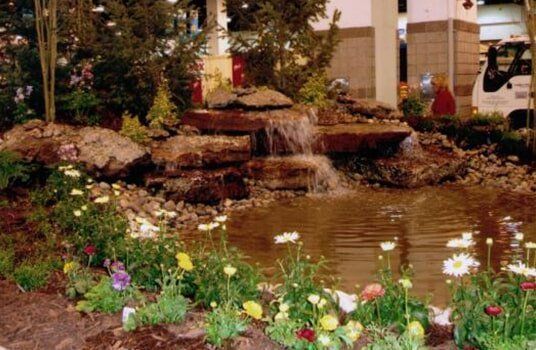 Small pond with waterfall and flowers, located in an indoor space.