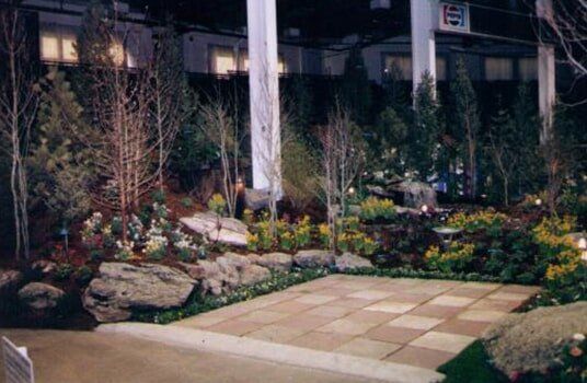 Garden display with stone patio, boulders, and various trees and shrubs.