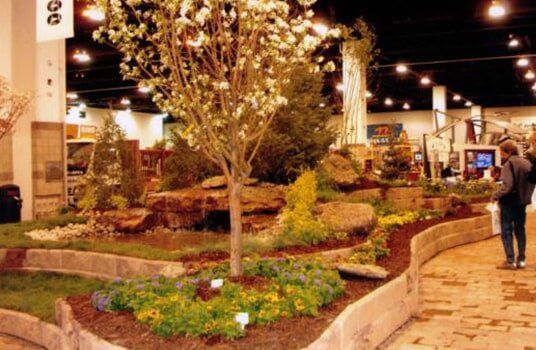 A landscaped garden display with a tree, rocks, and flowers; a person stands nearby.