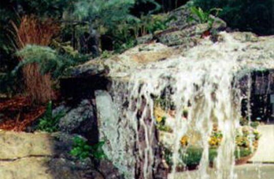 Waterfall cascading over rocks with plants in the foreground.