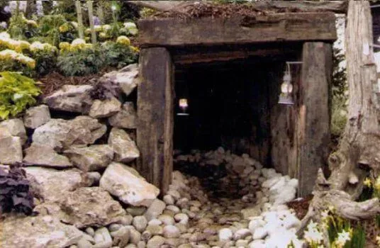 Wooden mine entrance in garden, rocks, and lanterns, leading to dark interior.
