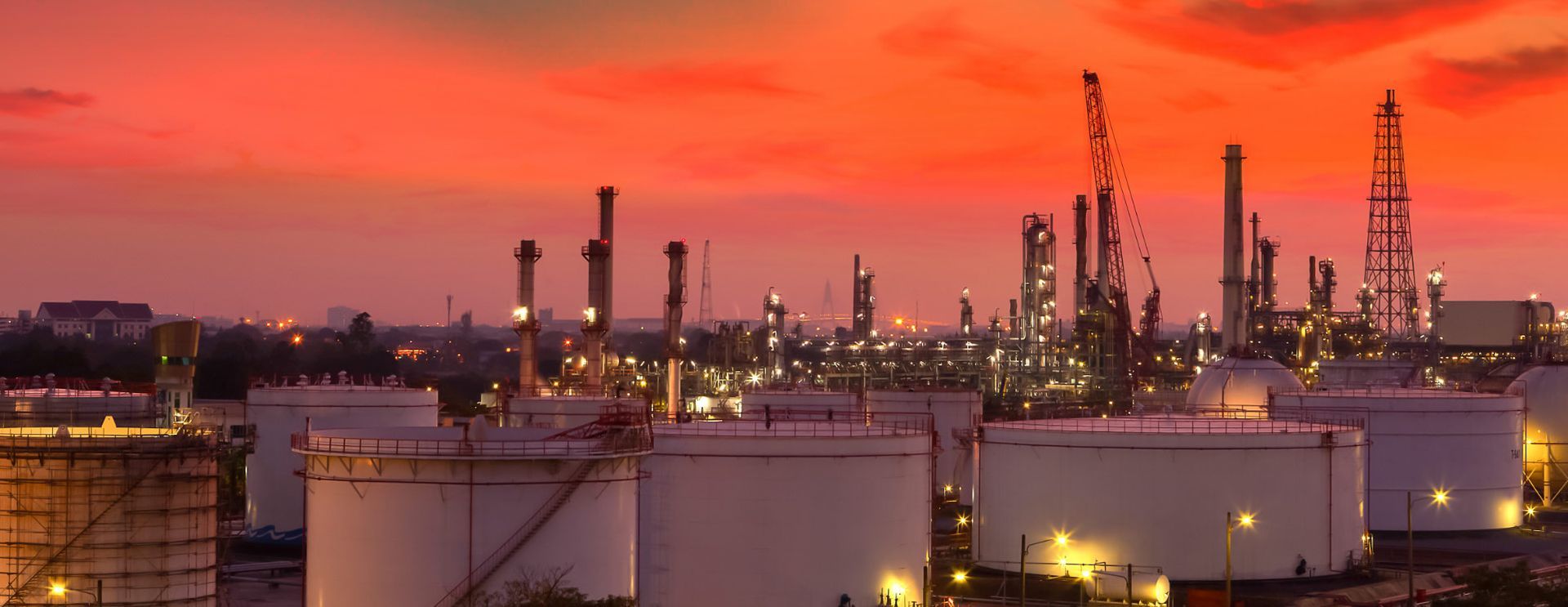 A large oil refinery is lit up at night with a sunset in the background.