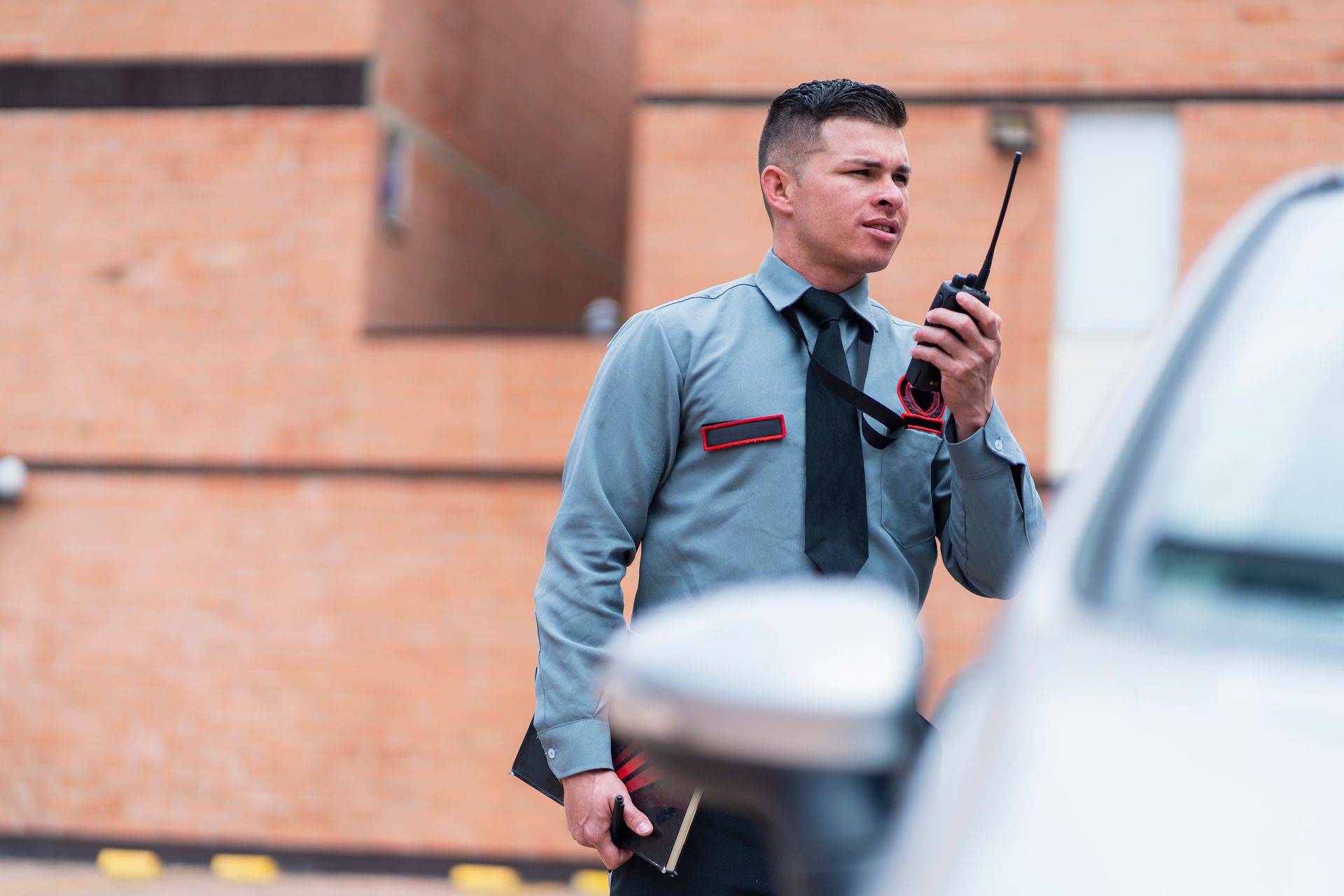 A security guard is talking on a walkie talkie next to a car.
