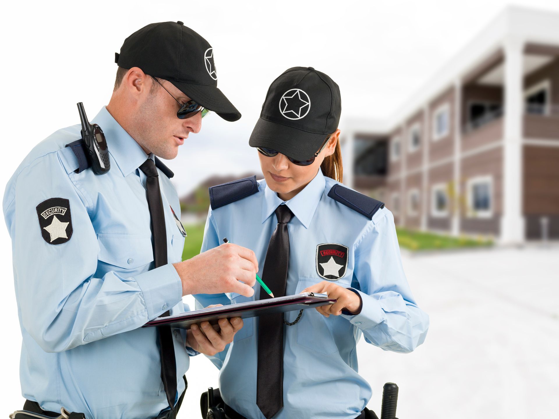 Two security guards are looking at a clipboard in front of a building.