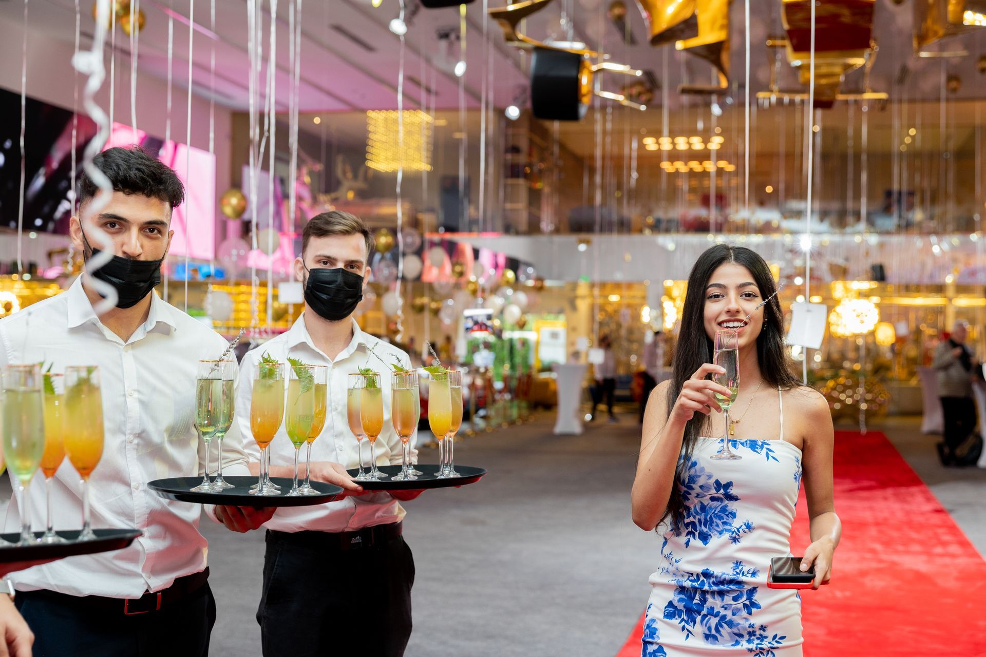 a woman is standing next to two waiters holding trays of champagne glasses .