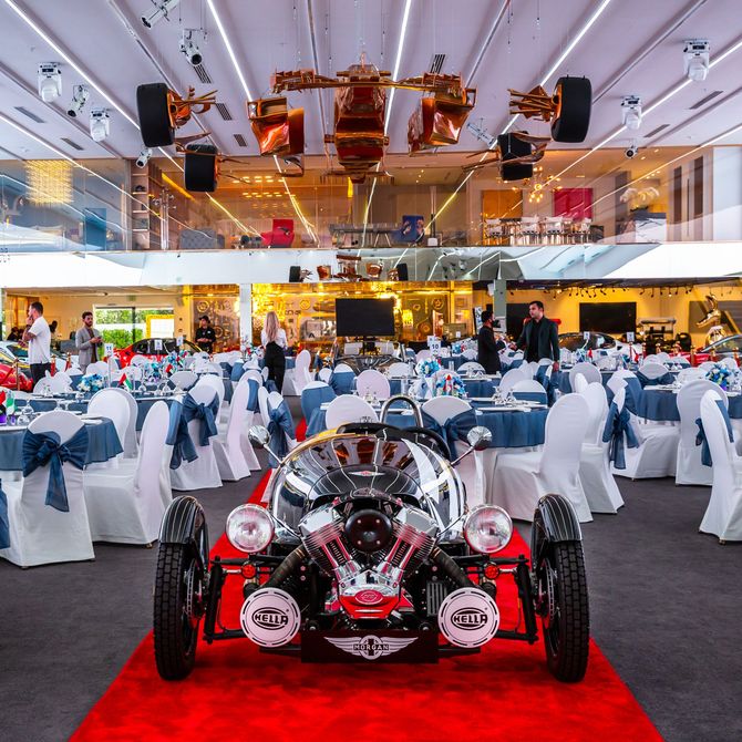 a car is parked on a red carpet in a room with tables and chairs