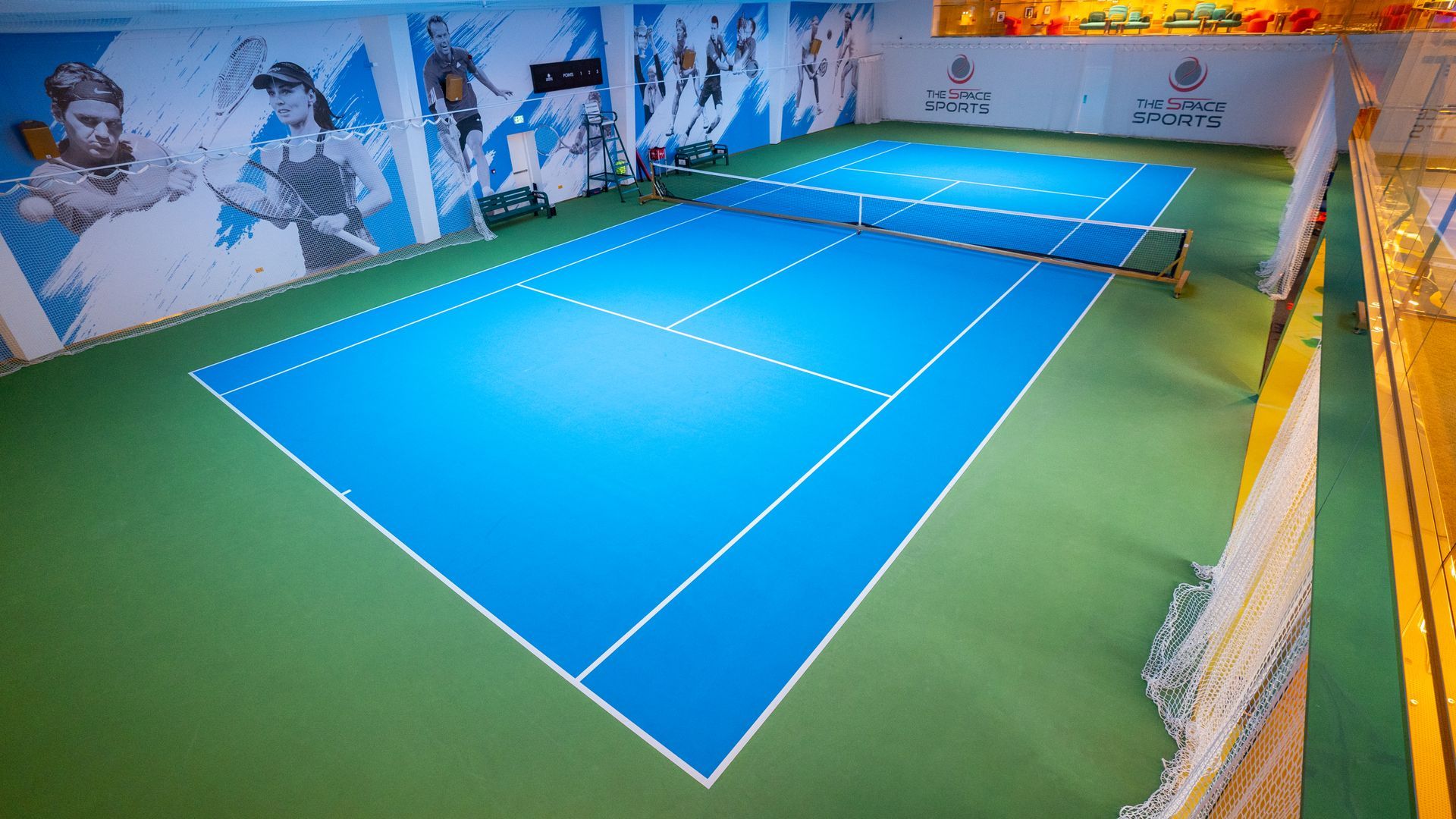 an indoor tennis court with a blue court and a green court .