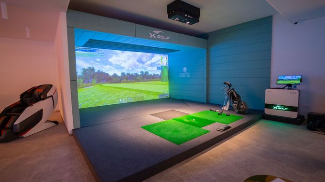a golf simulator in a living room with a golf bag and a computer .