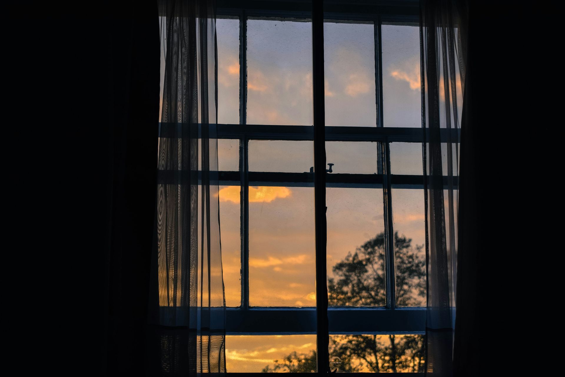 Una vista de una puesta de sol a través de una ventana con cortinas.