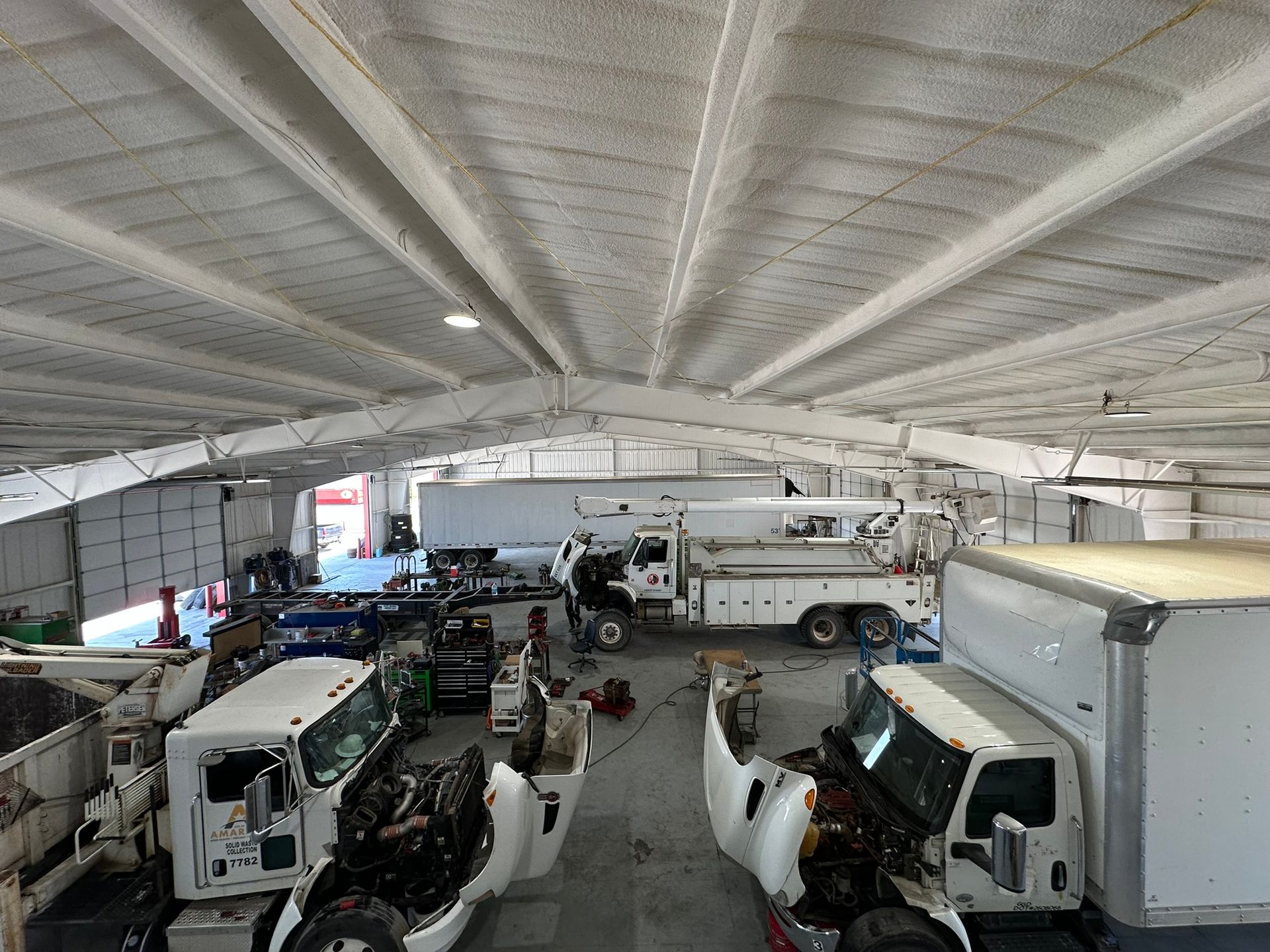 A large warehouse filled with trucks and trailers being worked on.
