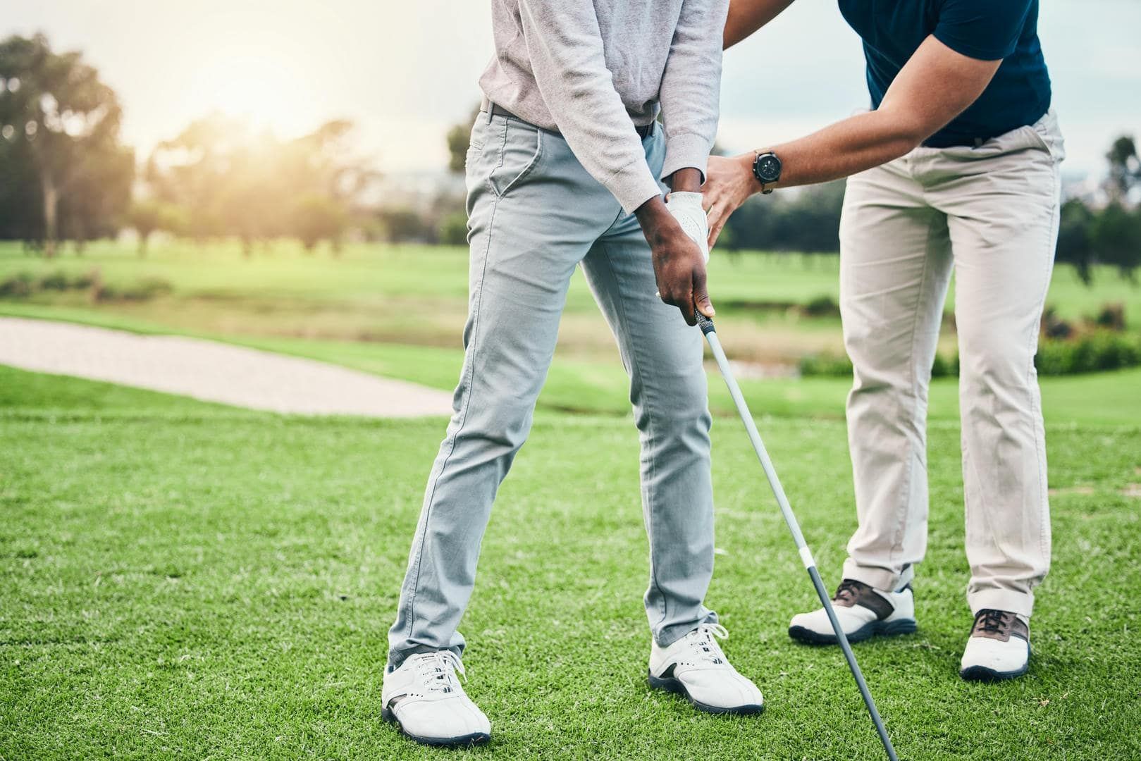 A man is teaching another man how to play golf on a golf course.