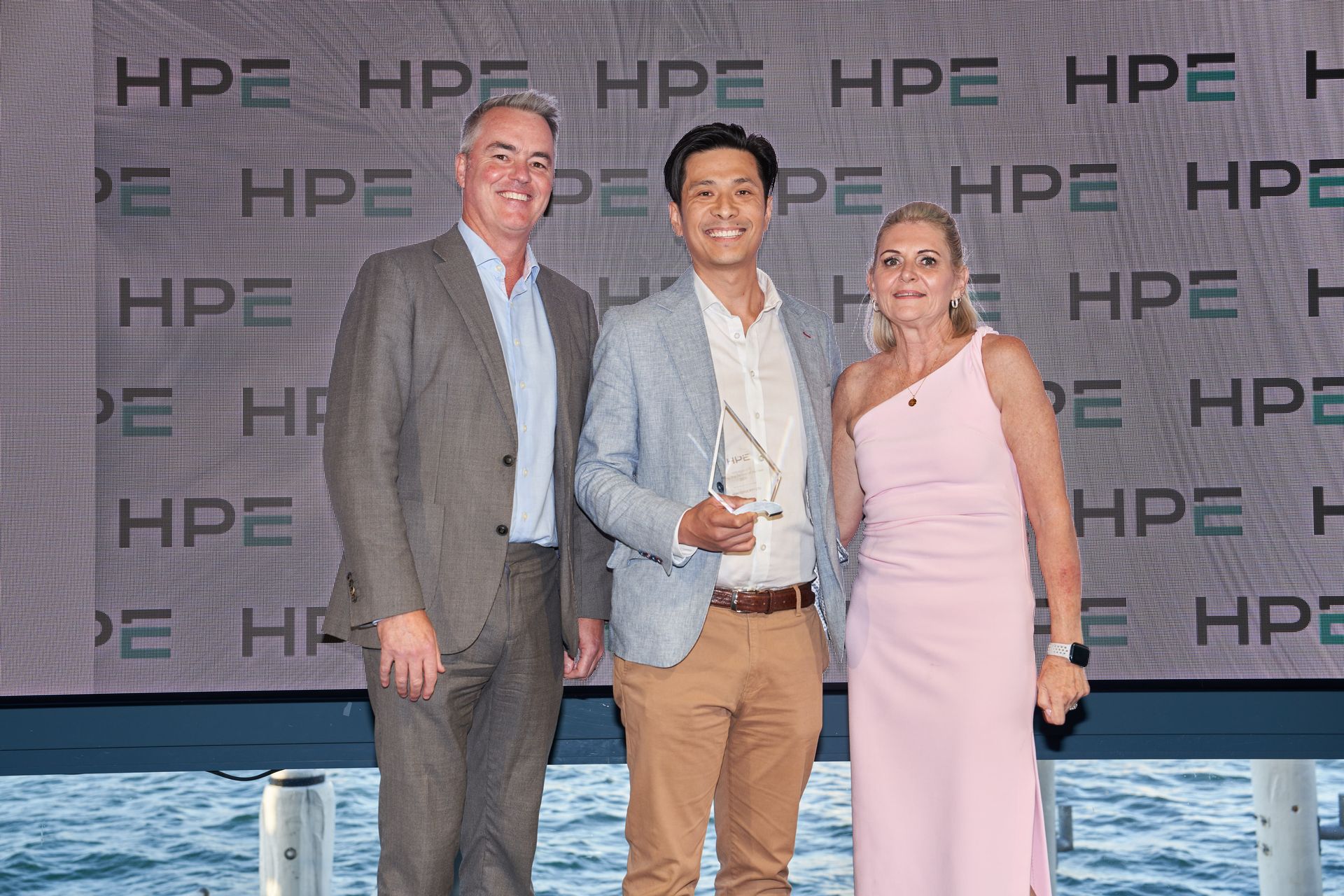 Three people pose, the middle person holds an award.