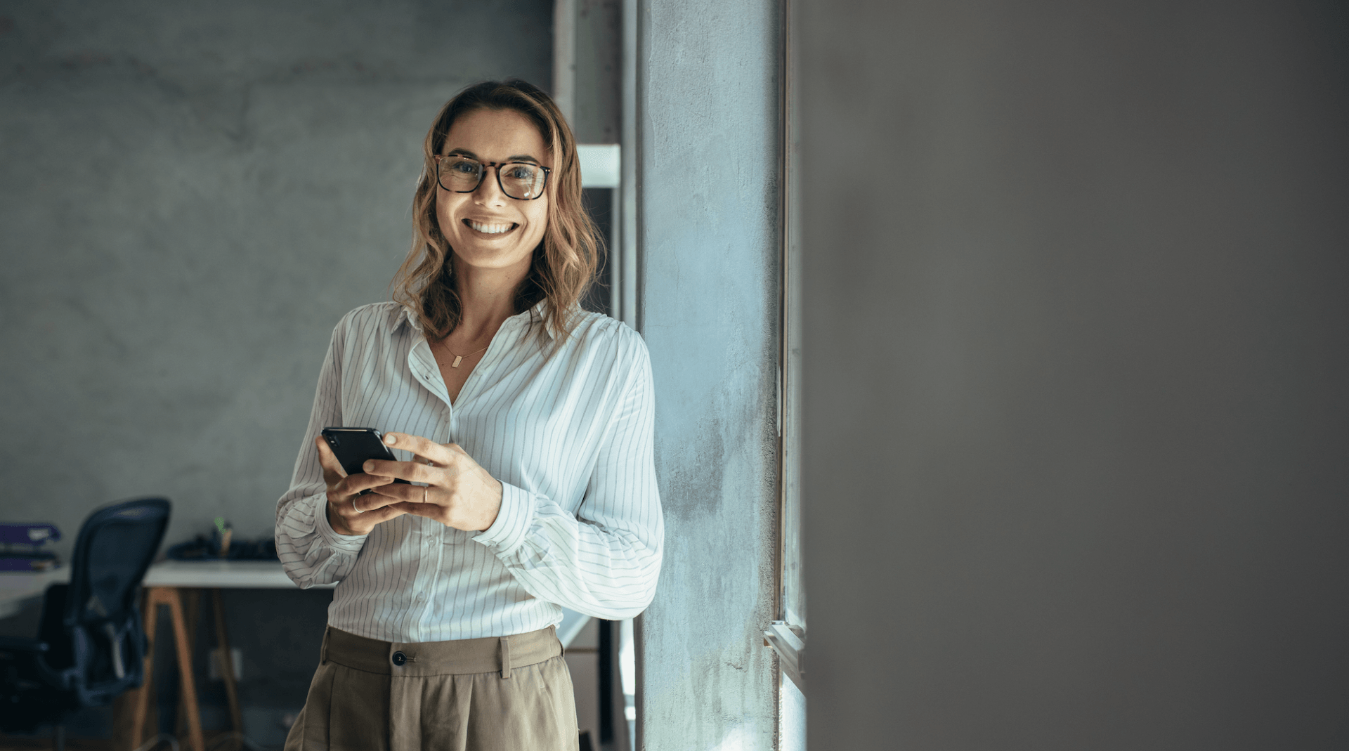 A woman is standing in front of a window holding a cell phone.