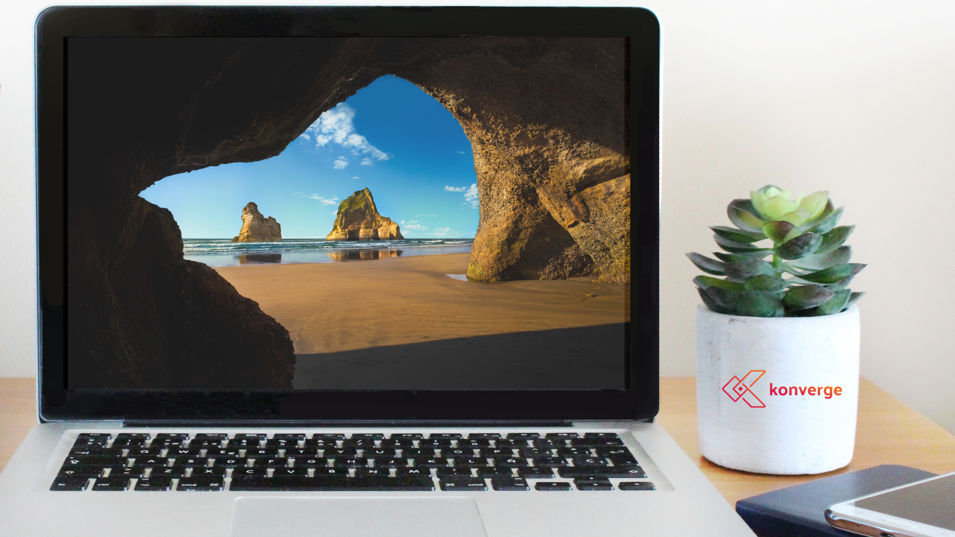 Laptop displaying a beach scene framed by rocks, with a potted succulent on the desk.