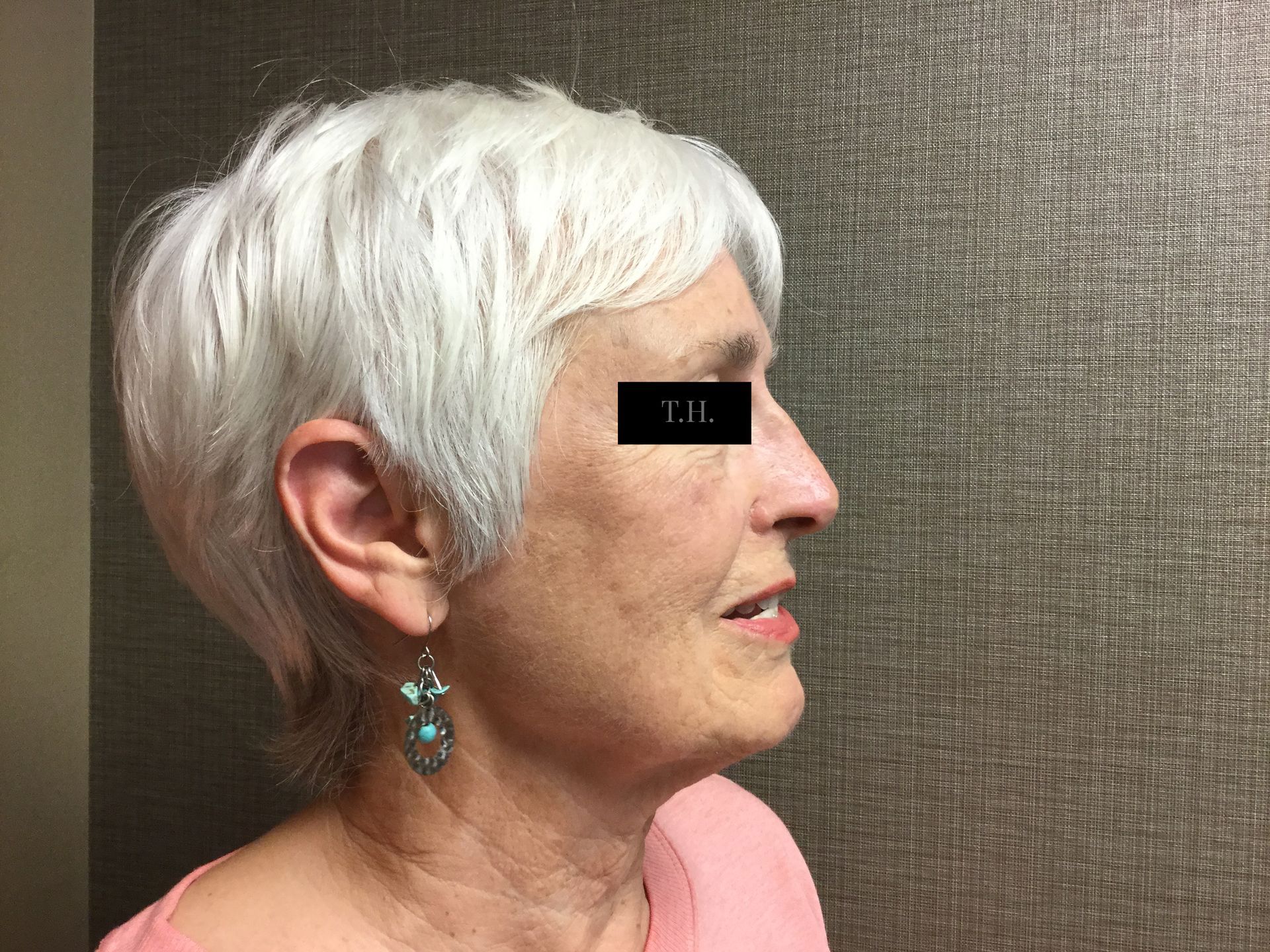 A woman with white hair and earrings is standing in front of a wall.