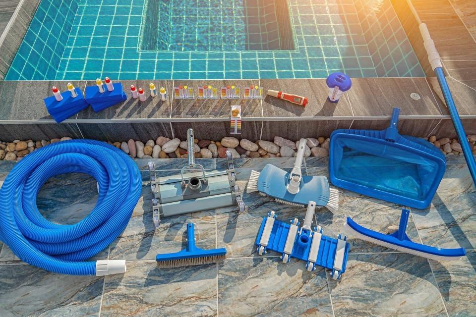 Pool cleaning supplies arranged on a tiled surface beside a swimming pool.