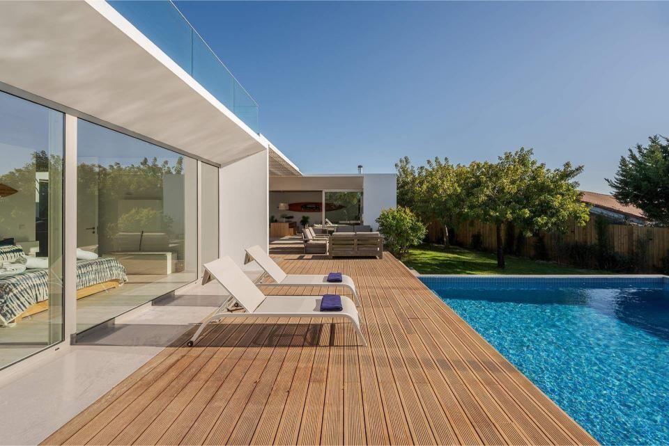 Modern home with a pool and wooden deck, two lounge chairs, and blue sky.