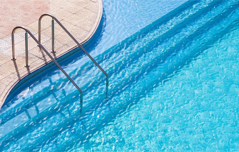 Pool with metal ladder and beige edge, water's surface reflects sunlight with blue ripples.