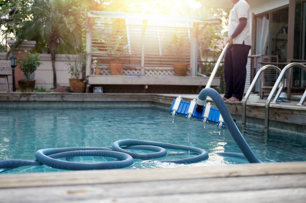 Person cleaning a swimming pool with a long-handled brush on a sunny day.