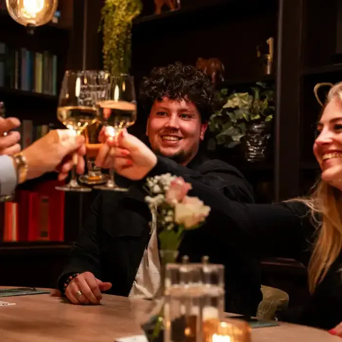 een groep mensen zit aan een tafel te proosten met wijnglazen.