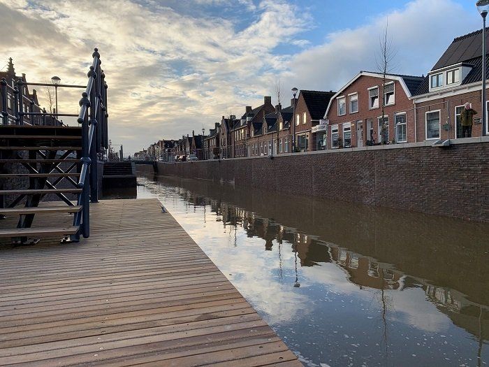een rij huizen langs een rivier met op de voorgrond een houten steiger.