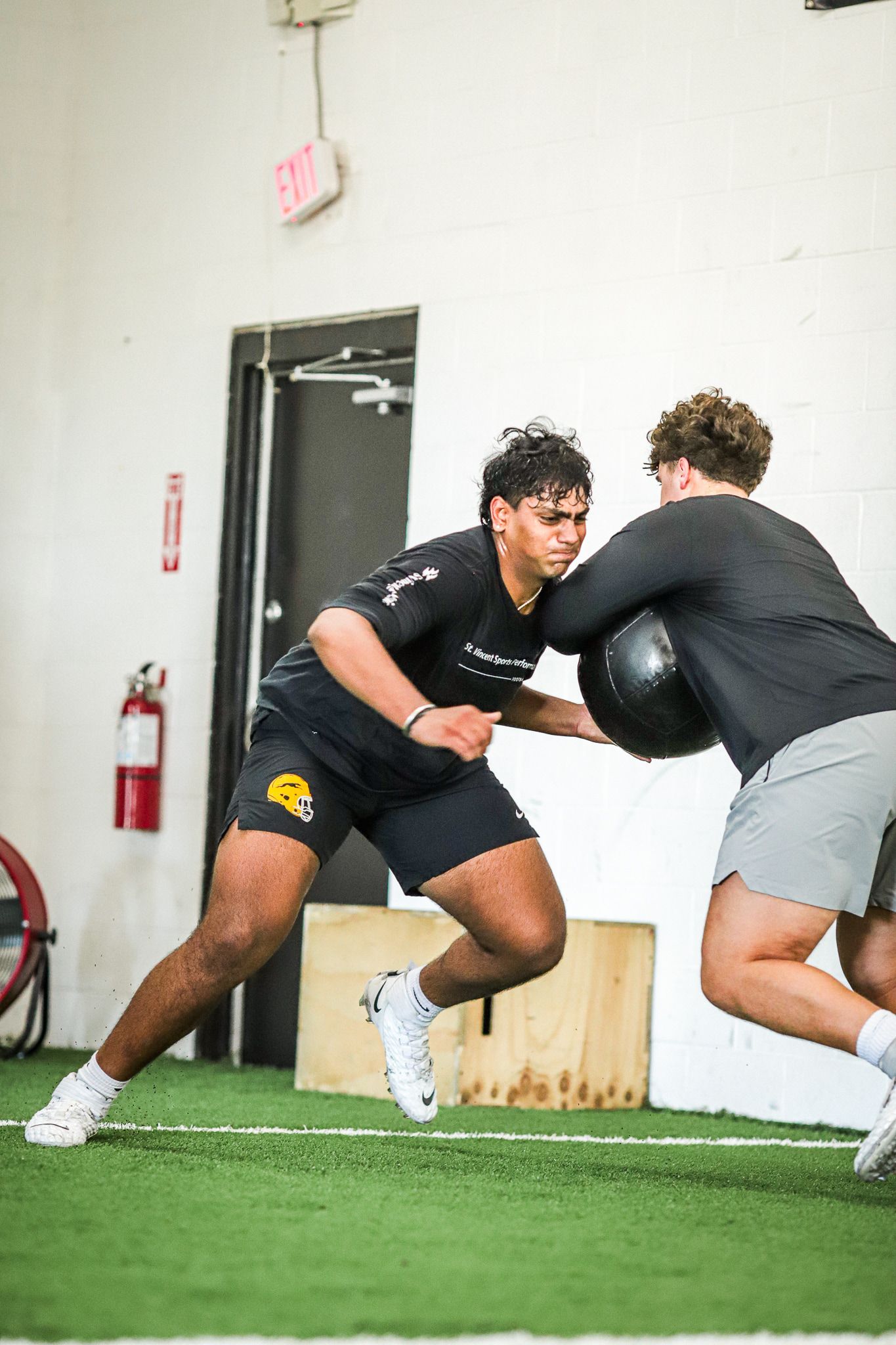 Two men training indoors with a medicine ball. One pushes the ball, the other resists.